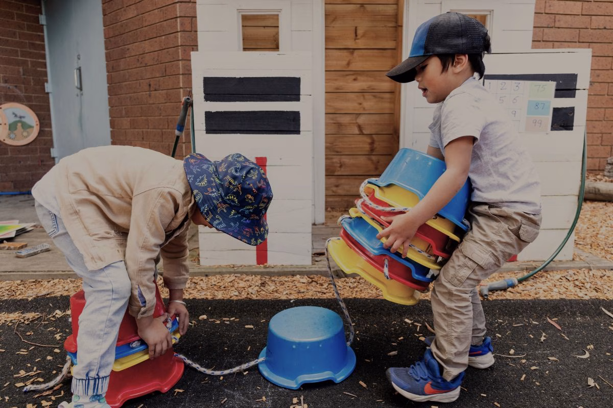 two-childrens-working-together-to-stack-colourful-tubs.avif